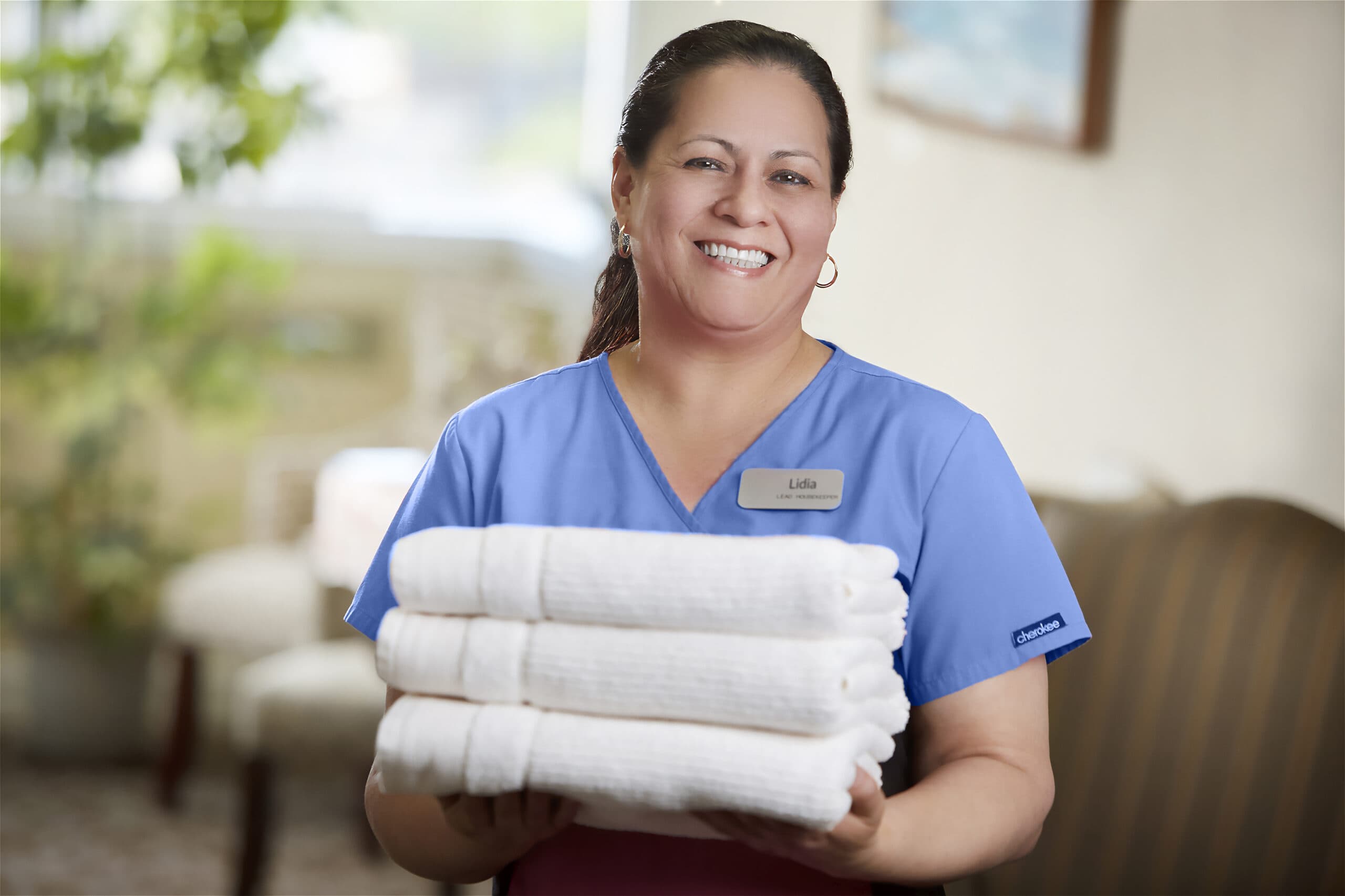 A smiling residential living employee holds a stack of towels.
